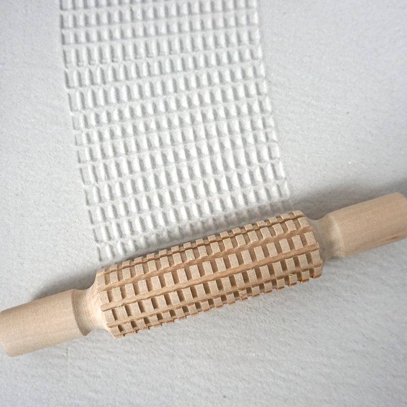 Wooden patterned rolling pins creating textured designs on clay surface