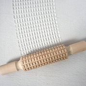 Wooden patterned rolling pins creating textured designs on clay surface