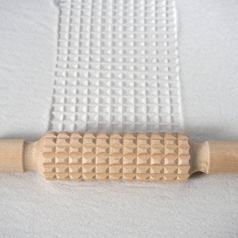 Wooden patterned rolling pins creating designs on clay surface