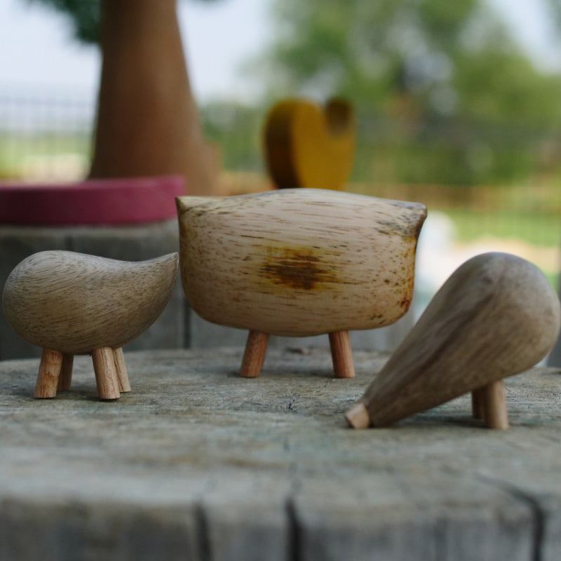 Three handmade fair trade wooden pebble animals with smooth, natural grain textures standing on a rustic wooden surface.