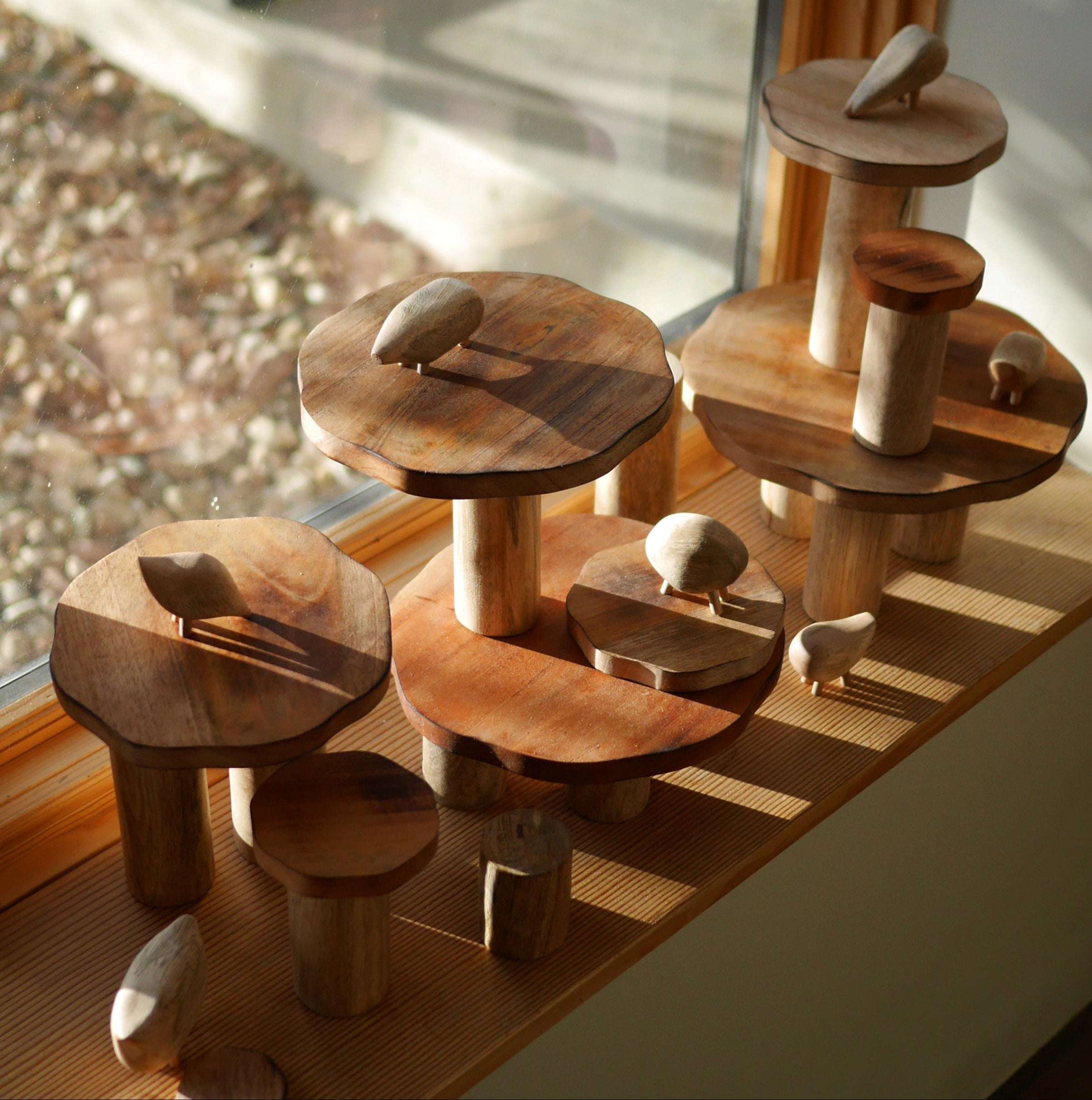 Handmade wooden pebble animals and tiered mushroom-shaped platforms on a sunny windowsill.