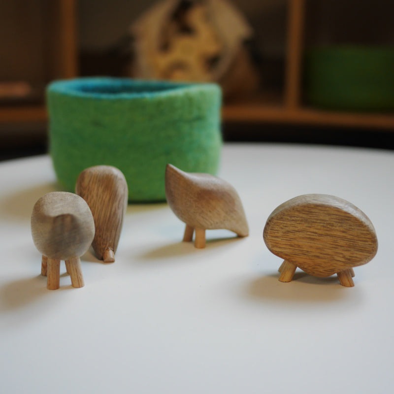 Handmade fair trade wooden animal pebbles with smooth, natural wood grain and small peg legs on a white surface.