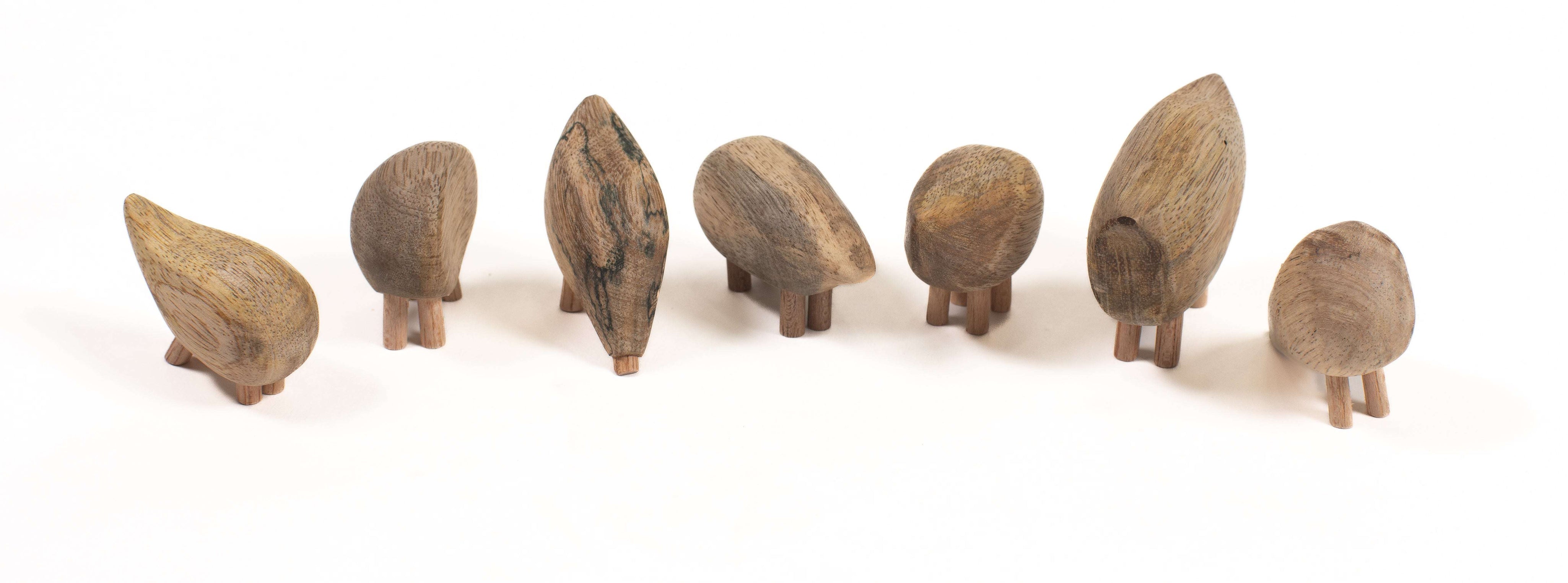 Handmade fair trade wooden pebble animals with smooth, natural wood grain and small peg legs on a white background.