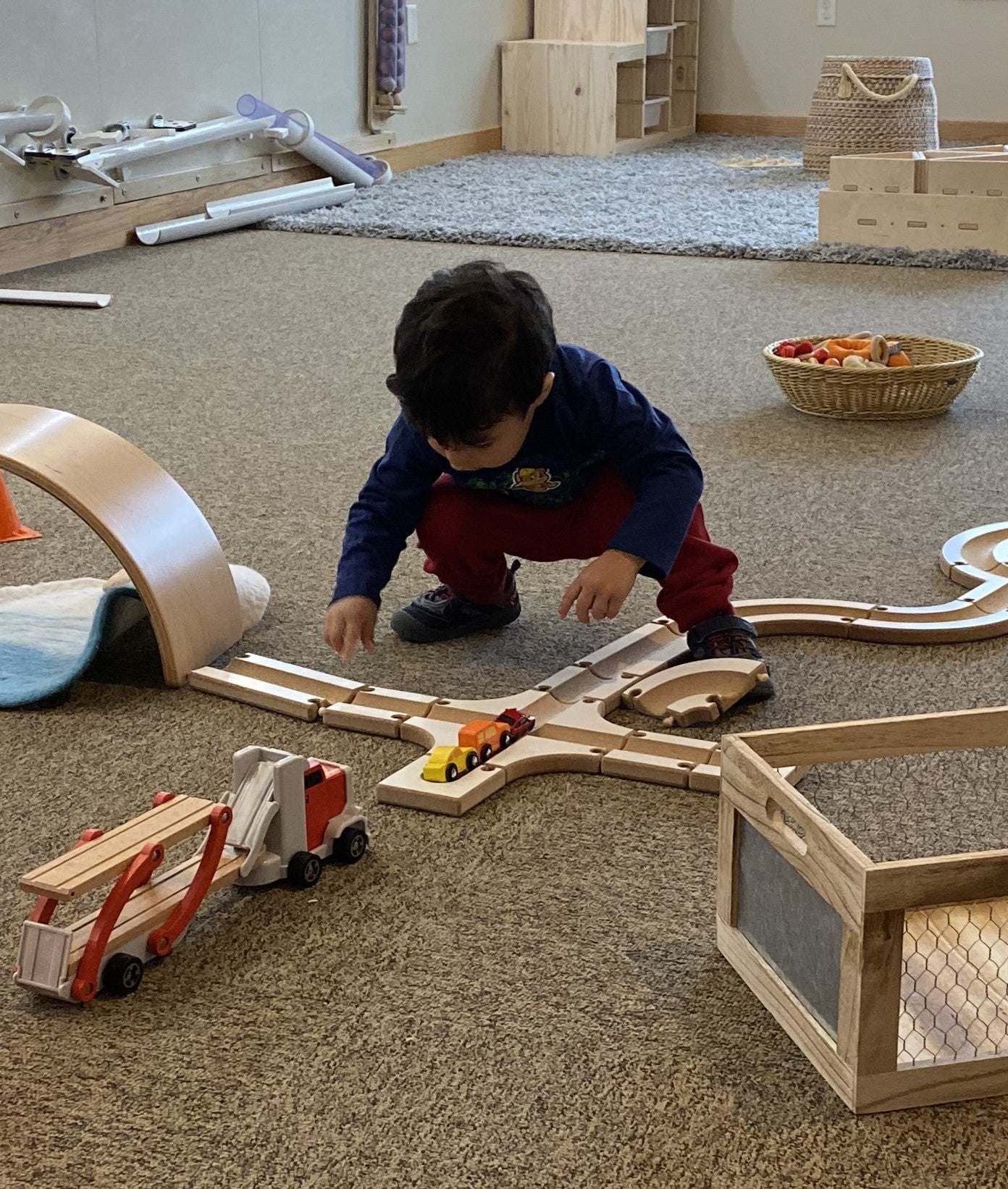 Child playing with modular wooden puzzle ball track pieces and toy cars on a carpeted floor.