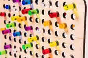 Light-colored birch wood pegboard featuring colorful, translucent acrylic pegs in various vibrant shades.