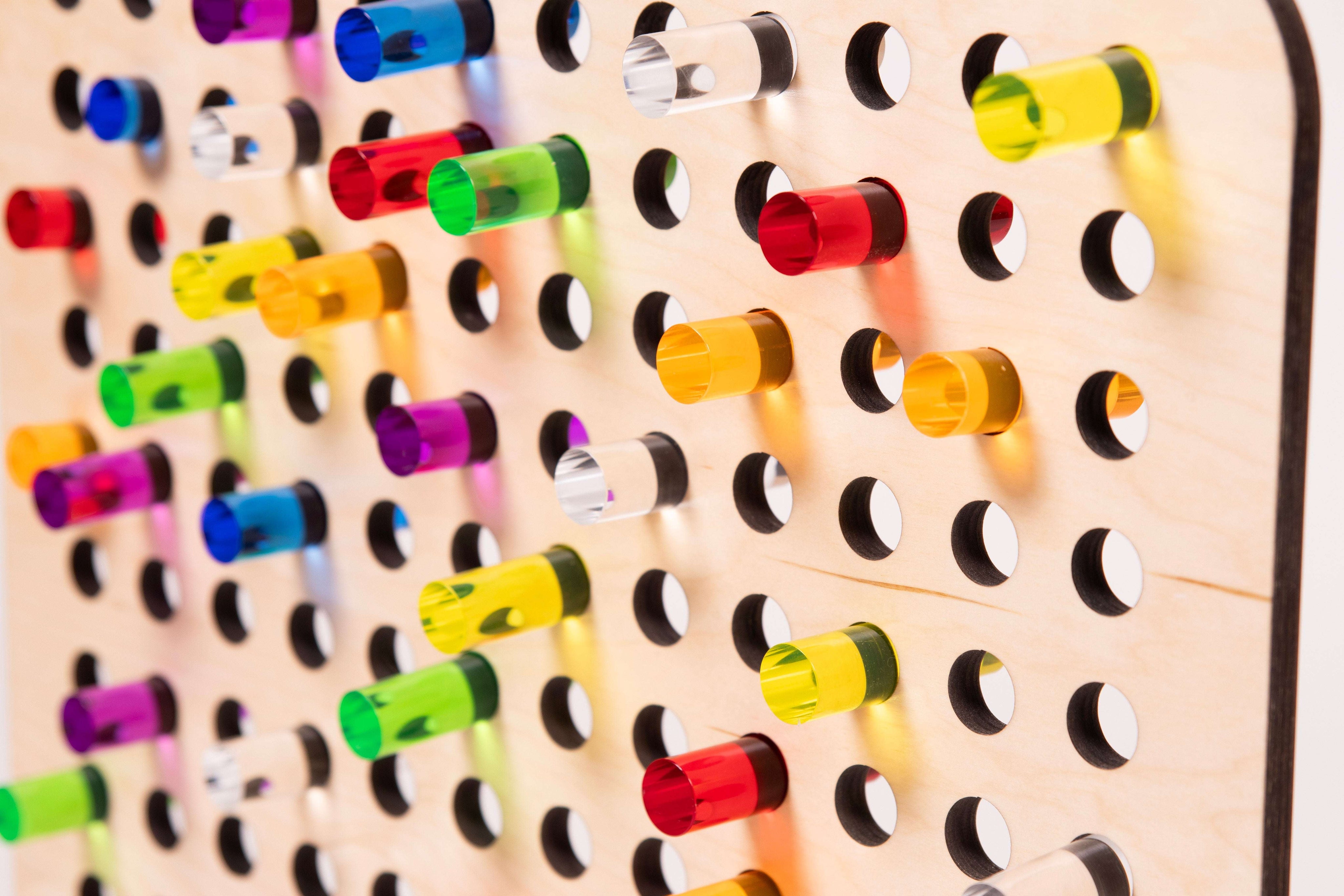 Light-colored birch wood pegboard featuring colorful, translucent acrylic pegs in various vibrant shades.