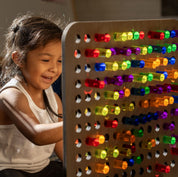 Child playing with a birch wood rainbow pegboard featuring colorful, light-catching transparent acrylic pegs.
