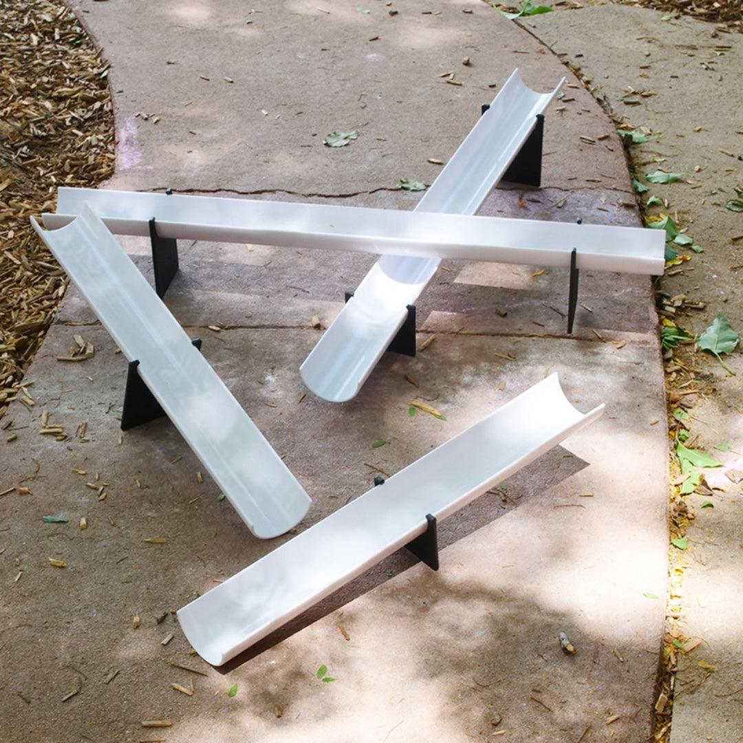 White plastic ramps with black fulcrum feet arranged on a concrete path for STEM play.