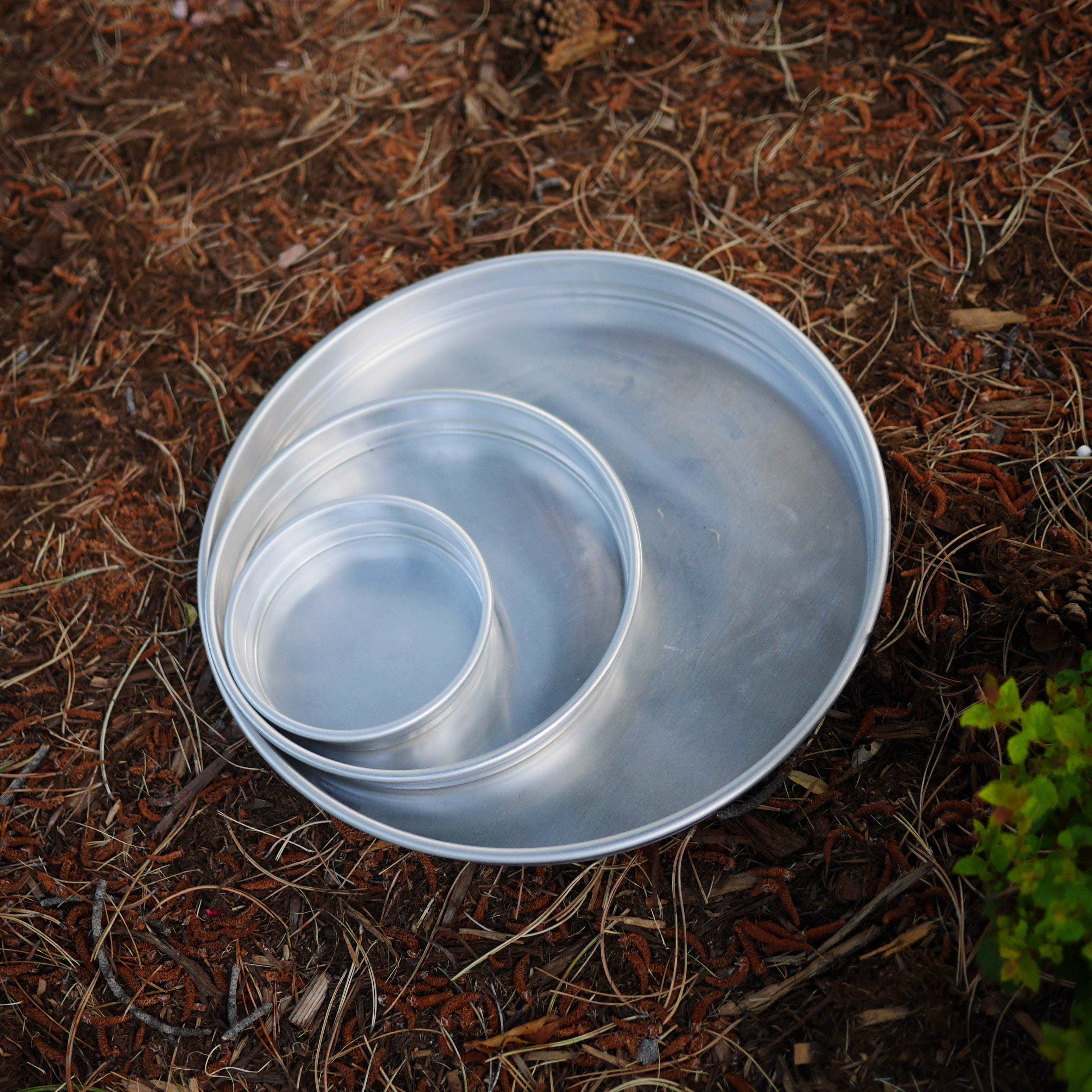 Set of three nesting round silver metal trays placed on a natural outdoor ground surface.
