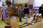 Children playing with a wooden Rubber Ramp Tower set featuring black tracks, ball storage, and elevated ramp configurations.