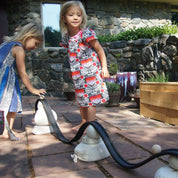 Two girls playing with a flexible black rubber ramp supported by white sandbags on a stone patio.