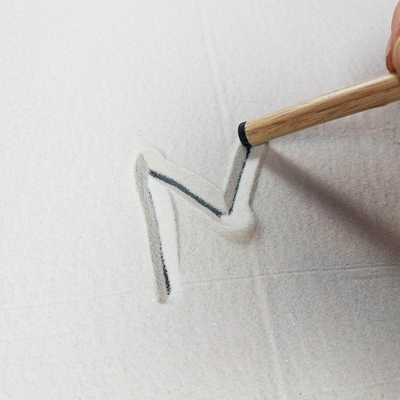 Wooden sand pencil drawing the letter M in fine white sand to practice pre-writing skills.