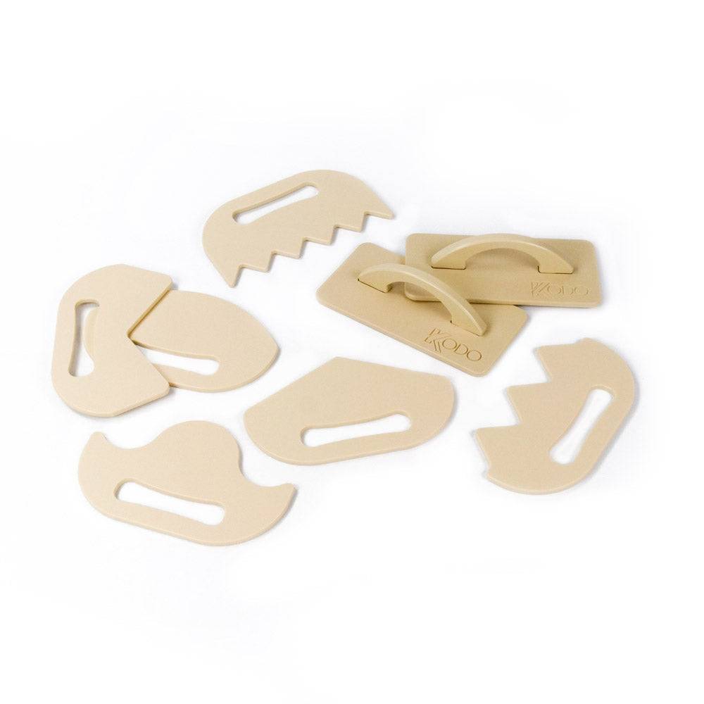 Eight-piece set of beige, ergonomic wooden sand shaping tools with various textured edges for creative play.