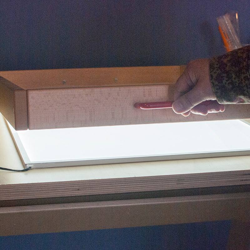 Slim rectangular LED light panel glowing brightly beneath a wooden sand tray for sensory play.