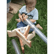 Child playing with a transparent plastic pipe and wooden stand for STEM exploration on green grass.