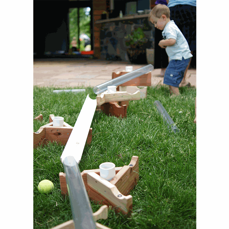 Child playing with a STEM see-through pipe and wooden stand set on a grassy lawn for outdoor sand and water play.