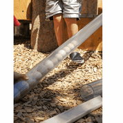 Transparent plastic pipe filled with wooden balls for STEM play, resting on a wood chip outdoor surface.