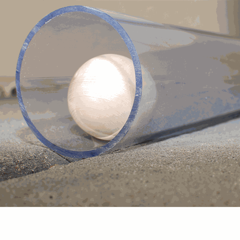 Clear, durable plastic pipe for STEM play with a white ball inside, resting on a sandy surface.