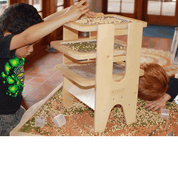 Children using a wooden Sift & Sort tower with three removable mesh screens to classify sensory materials by size.
