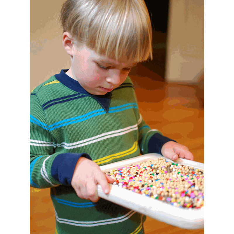 Child holding a white Sift & Sort screen filled with colorful sensory beads for size classification.