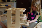 Child using a wooden Sift & Sort tower with three removable mesh screens to classify sensory materials by size.