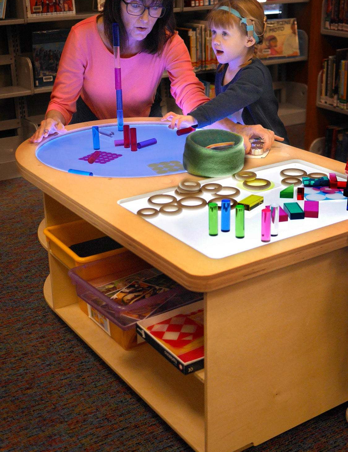 Teacher and child exploring a wooden Spectrum Light Lab table with circular and rectangular illuminated panels.