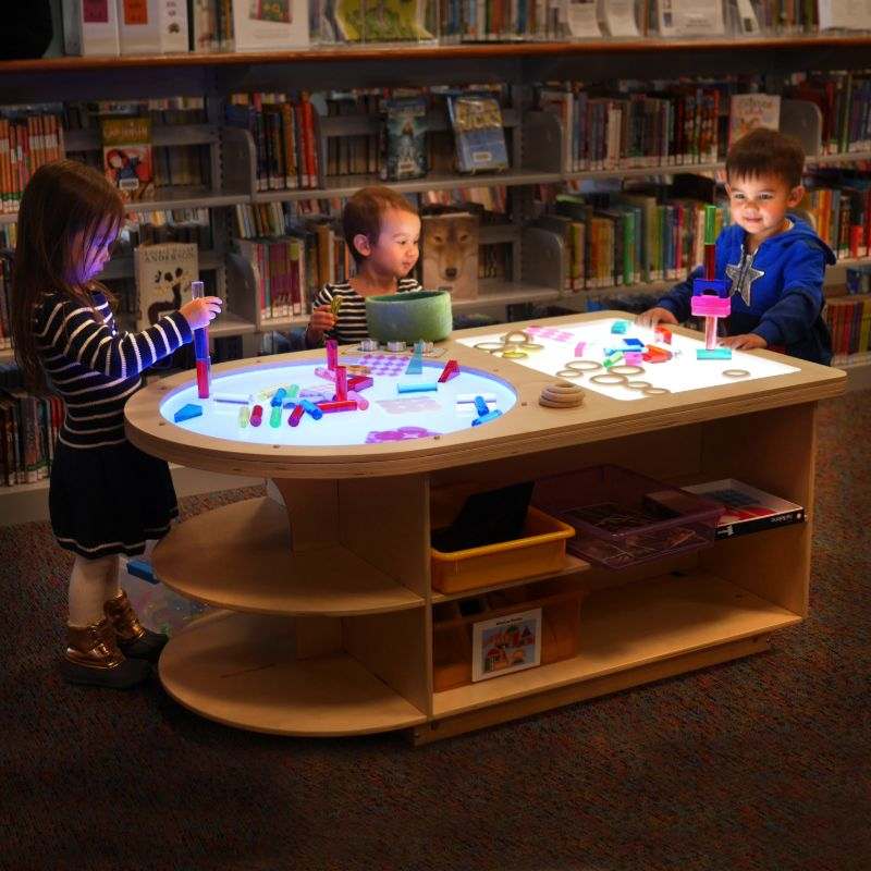 Children playing with colorful blocks on a wooden Spectrum Light Lab table with built-in storage in a library setting.