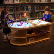 Children playing with colorful blocks on a wooden Spectrum Light Lab table with built-in storage in a library setting.