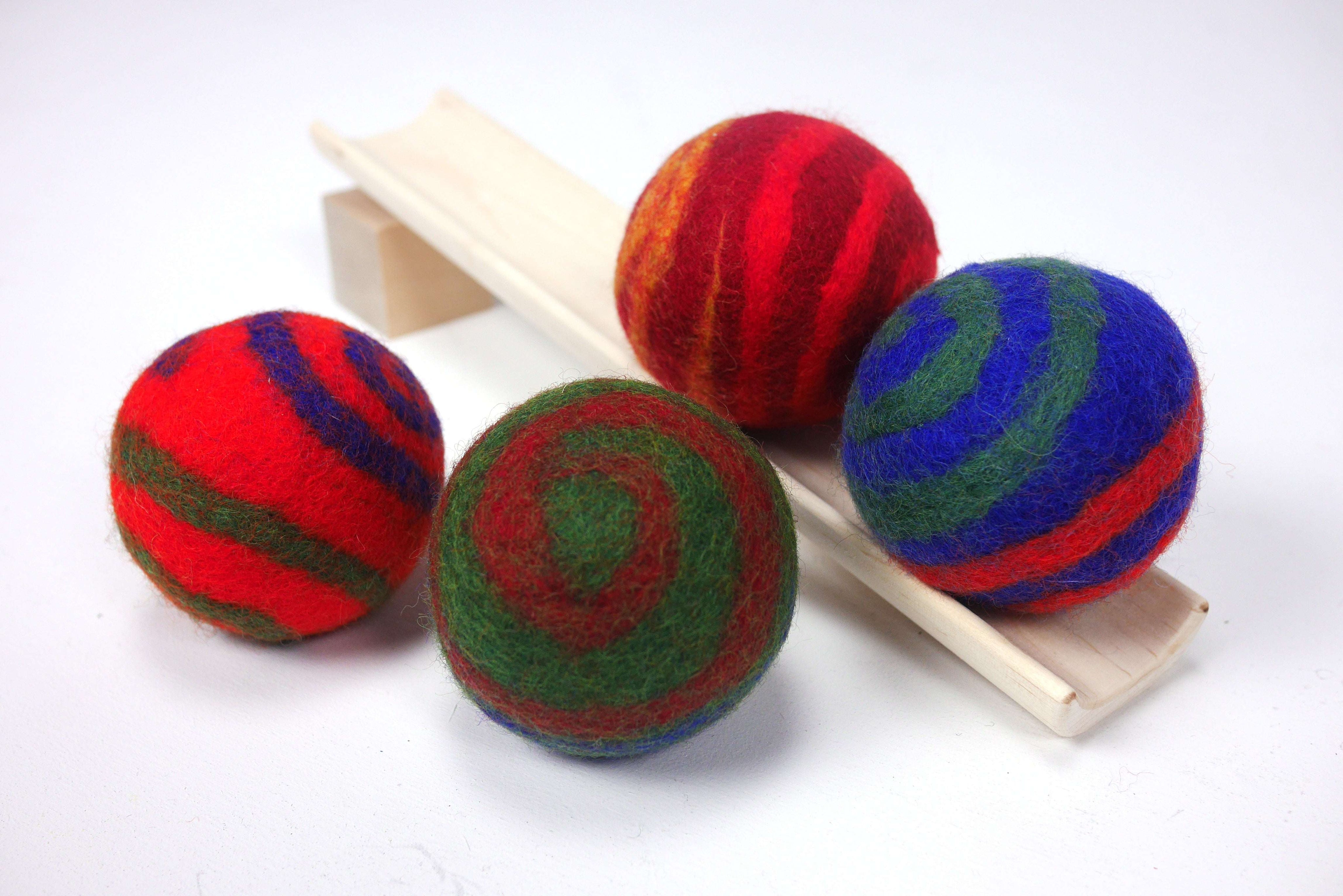 Four vibrant, felted wool balls with colorful spiral patterns resting on a small wooden ramp.