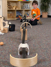 Child playing with black stacking tunnels and wooden arches on a carpeted floor to create a marble run system.