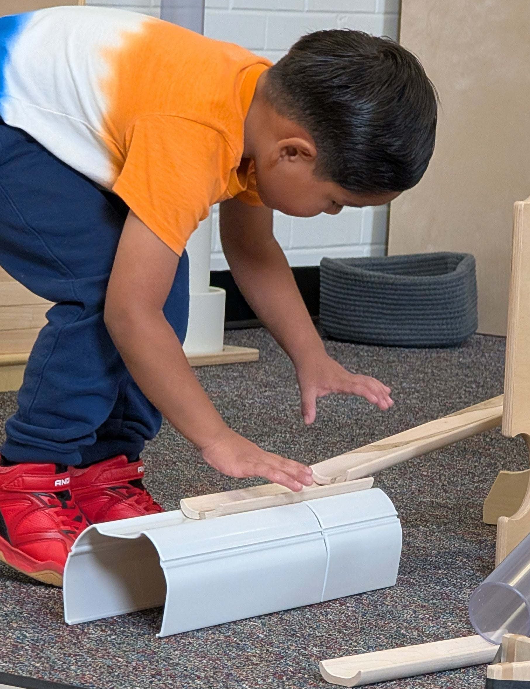 Child building with white plastic stacking tunnels and wooden ramps on a carpeted floor.