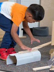 Child building with white plastic stacking tunnels and wooden ramps on a carpeted floor.