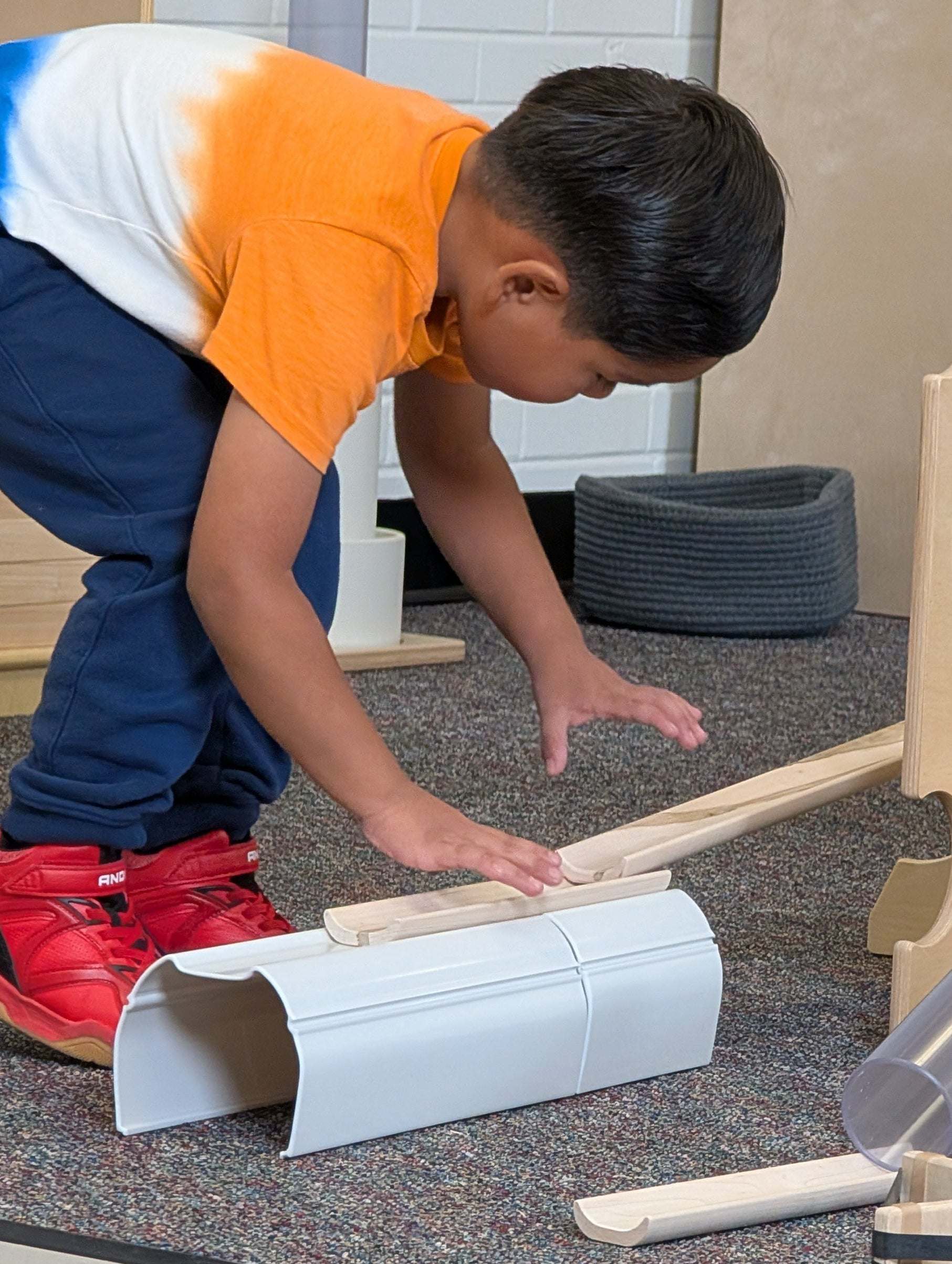 Child building with white plastic stacking tunnels and wooden ramps on a carpeted floor.