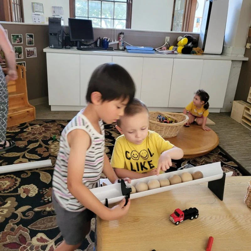 Children using black plastic Stop and Go Ramp Gates attached to a white Kodo ramp with wooden balls.