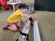 Child playing with black Stop and Go ramp gates clipped onto white plastic ramps holding wooden balls.