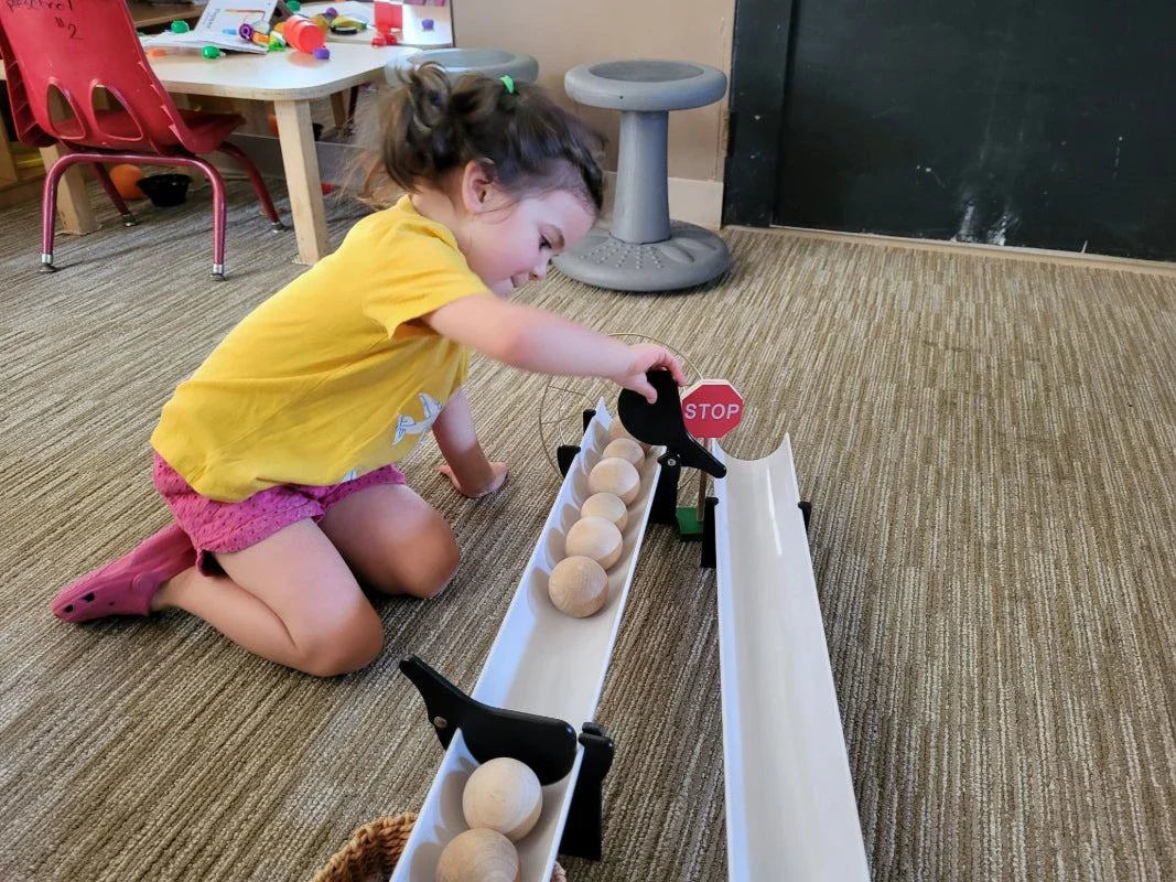 Child playing with black Stop and Go ramp gates clipped onto white plastic ramps holding wooden balls.