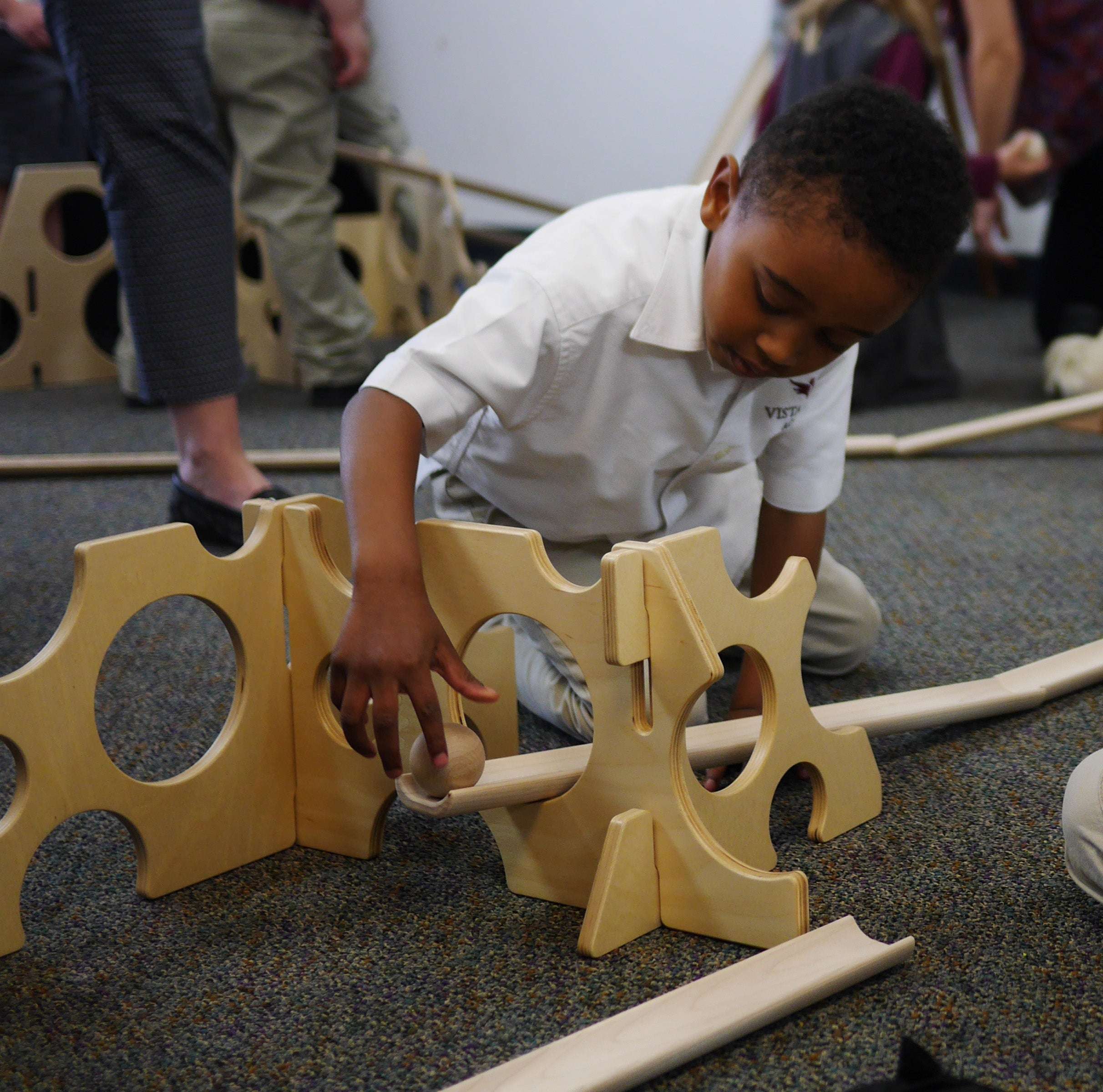 Child building a wooden ramp track with Swiss cheese-inspired stands featuring circular cutouts for STEM play.