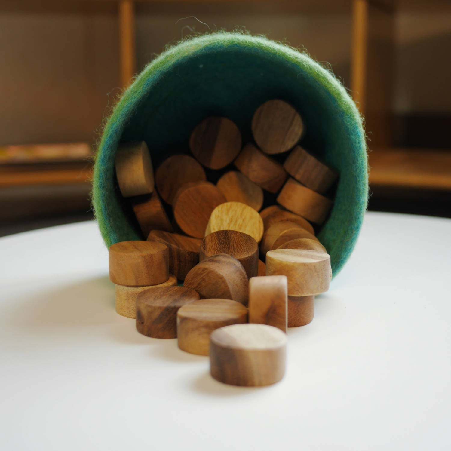 Smooth, polished teak wood slices spilling out of a green felt container onto a white surface.