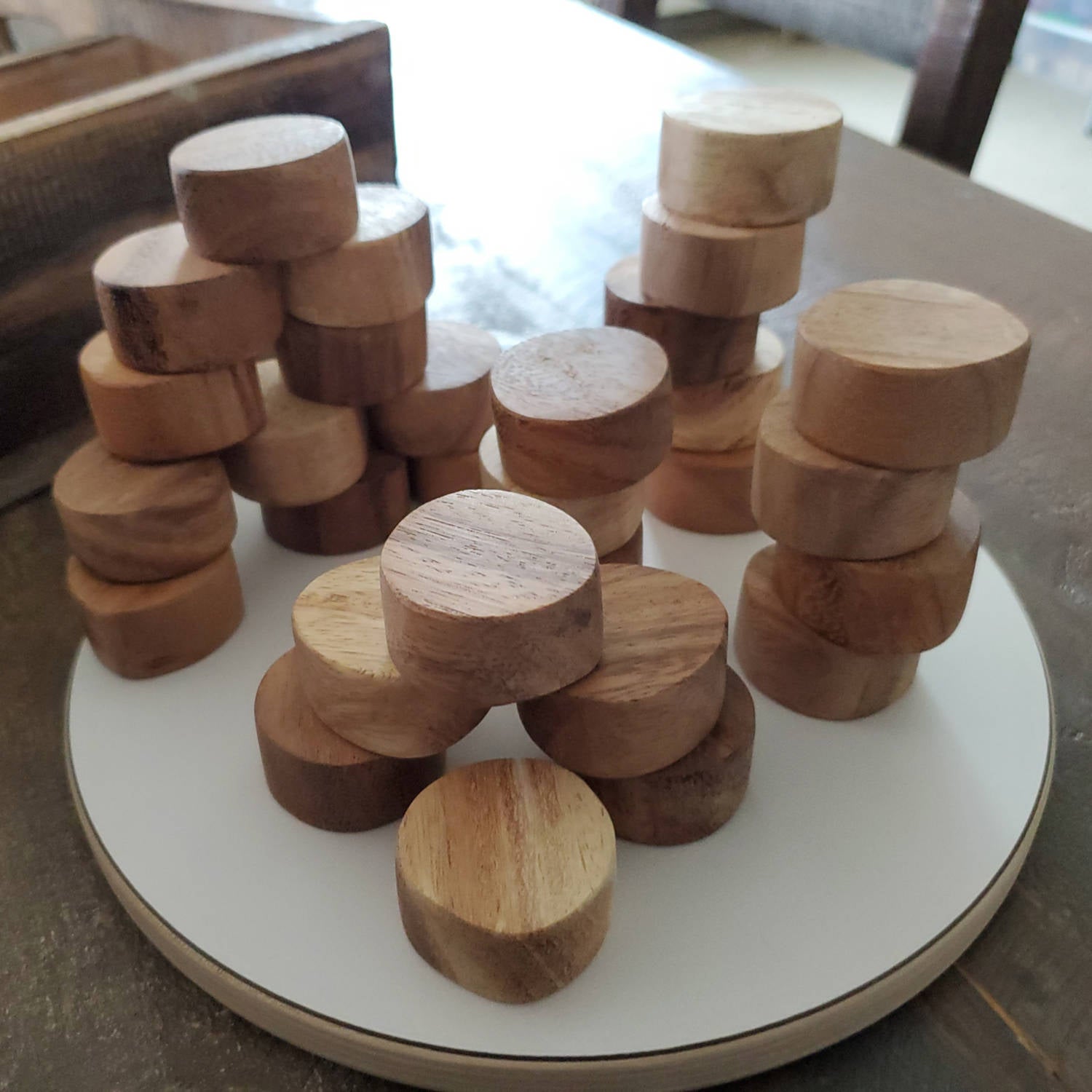 Smooth, polished teak wood slices stacked in small piles on a white circular tray.