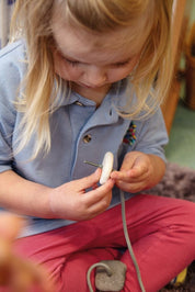 A young child threading a smooth, white tactile pebble onto a grey cord to develop fine motor skills.