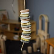 A stack of 16 tactile, multicolored threading pebbles in shades of gray, white, and tan, strung on a cord for sensory play.