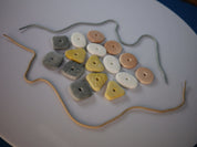 Set of 16 tactile threading pebbles in assorted shapes, colors, and textures with two threading laces on a white surface.