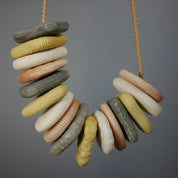 Set of 16 tactile threading pebbles in grey, yellow, white, and peach, strung on a cord for sensory and fine motor play.