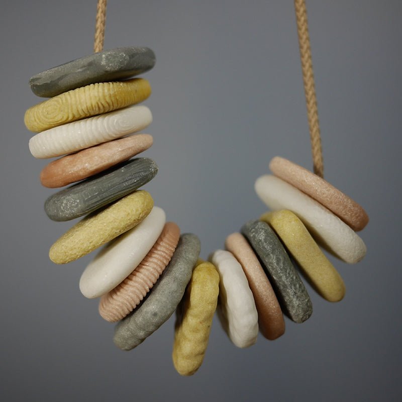 Set of 16 tactile threading pebbles in grey, yellow, white, and peach, strung on a cord for sensory and fine motor play.