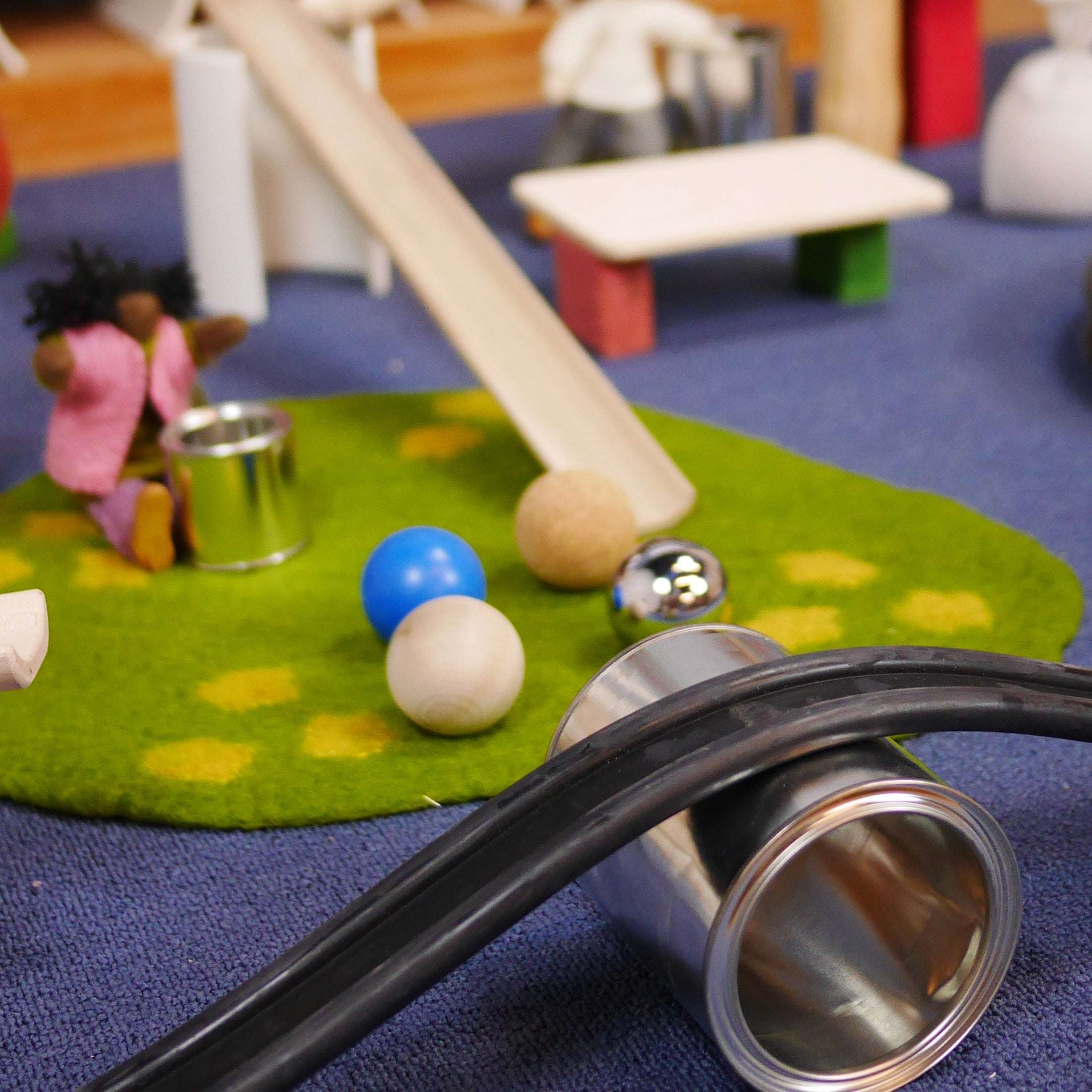 Shiny metal tins in various sizes used as open-ended play props alongside wooden balls and a toy ramp on a green rug.