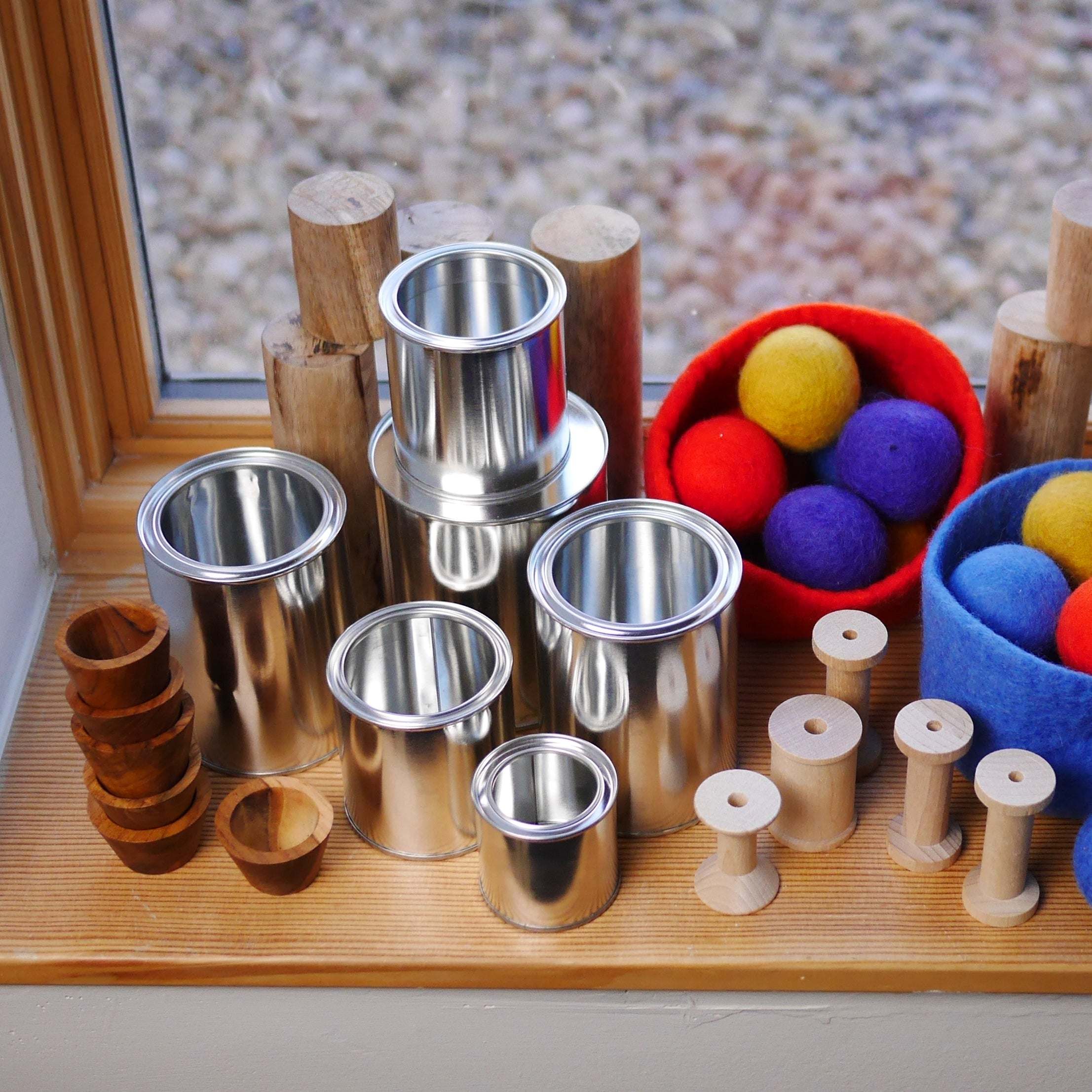 Set of 20 shiny silver metal tins in various sizes, arranged with wooden spools and colorful felt balls on a wooden windowsill.
