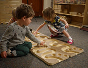 Toddlers playing with a wooden ball run featuring winding tracks and smooth spheres on a classroom floor.