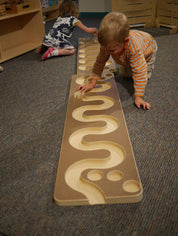 Toddlers playing with a wooden ball run featuring a winding, carved track on a carpeted floor.