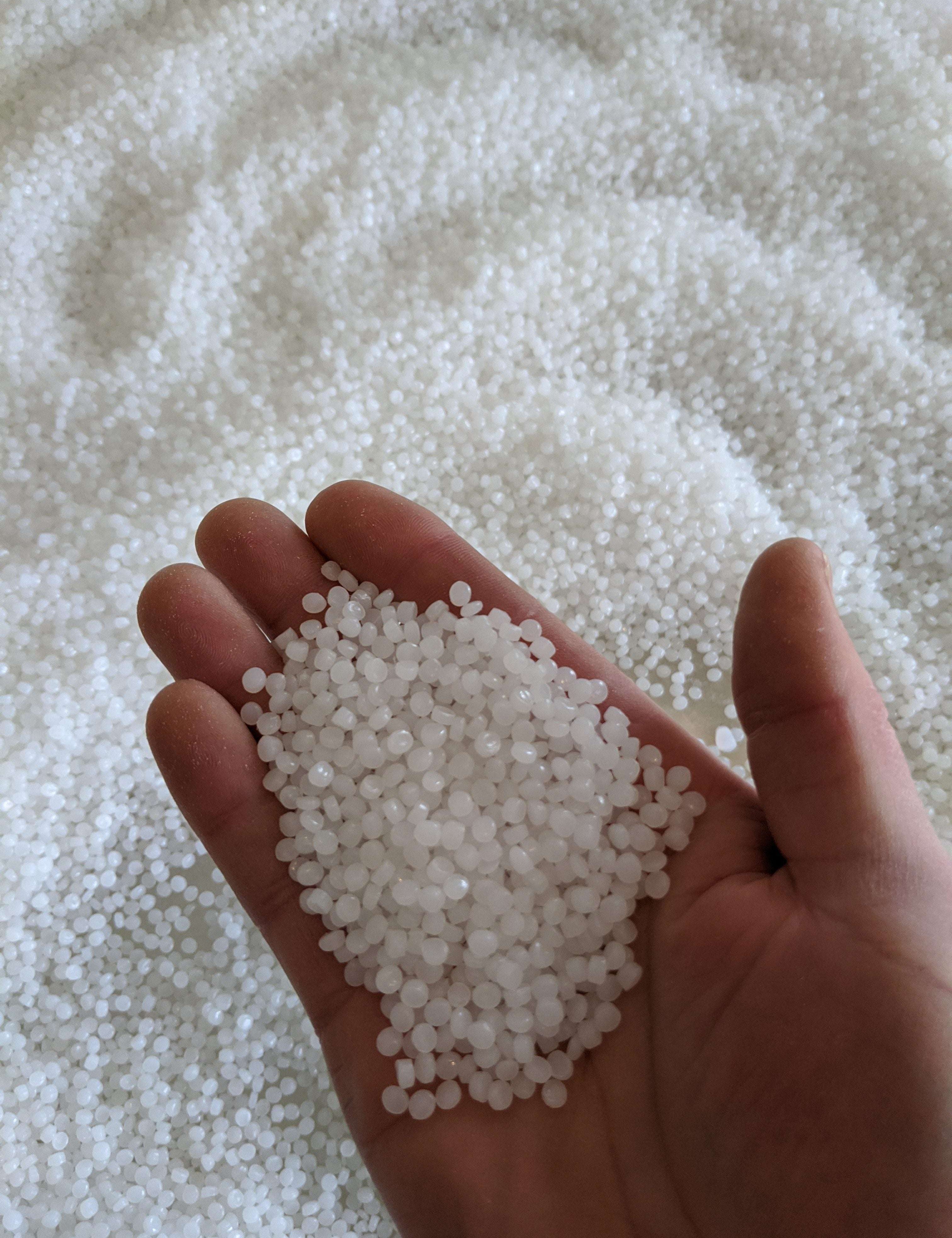 Handful of small, milky white translucent sensory beads held over a large pile of the same material.