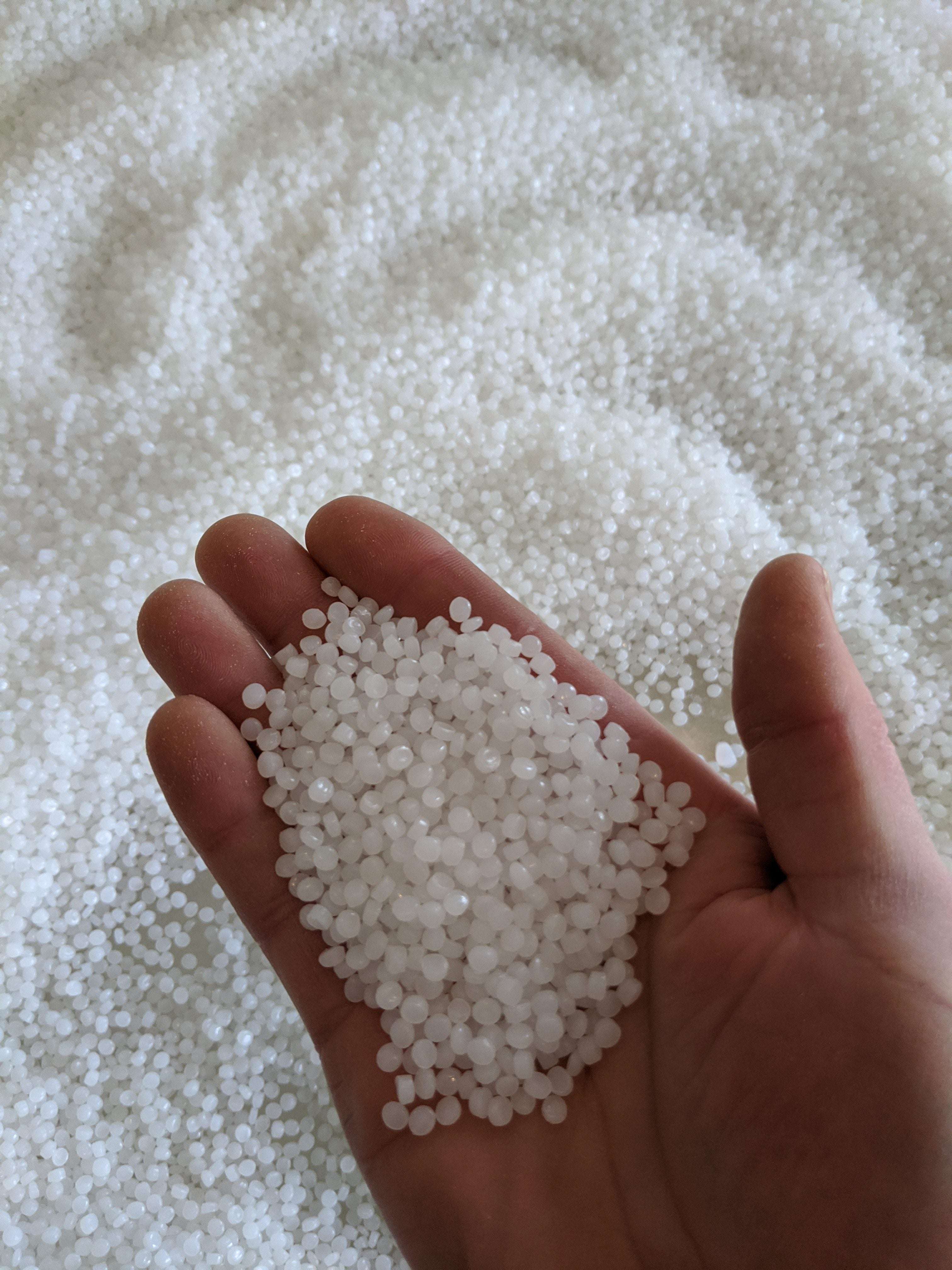 Handful of small, milky white translucent sensory beads held over a large pile of the same material.